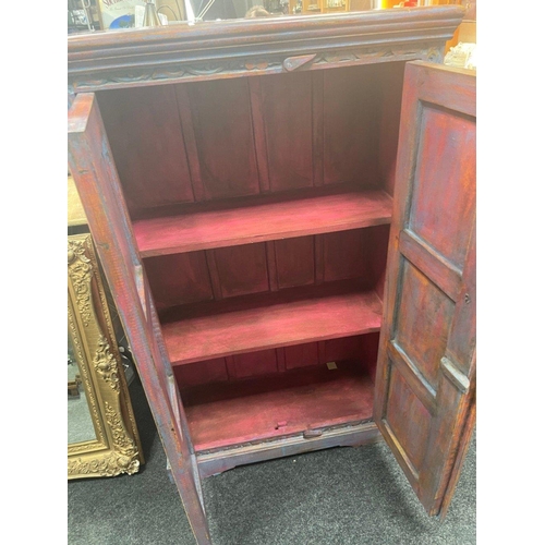 579 - A carved Indian cupboard with 3 internal shelves in coral pink with blue accents on the front, measu... 