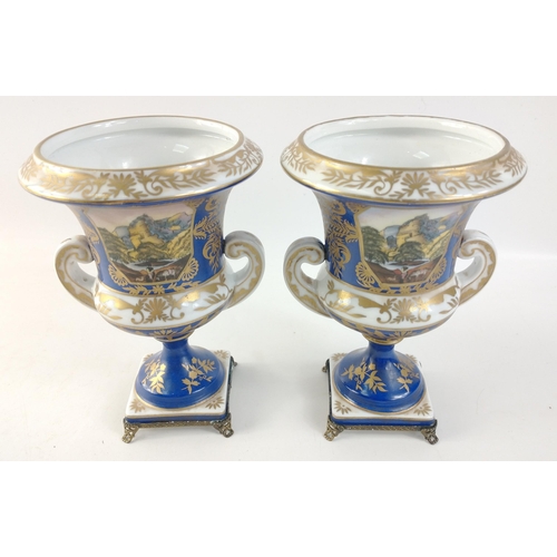 305 - A pair of twin-handled pedestal urns with metallic feet in blue with gilt highlights each standing a... 