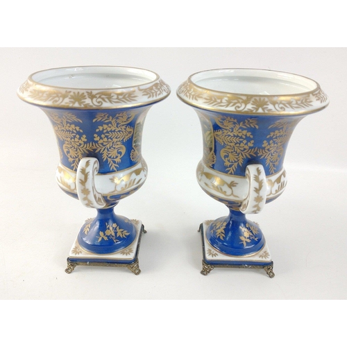 305 - A pair of twin-handled pedestal urns with metallic feet in blue with gilt highlights each standing a... 