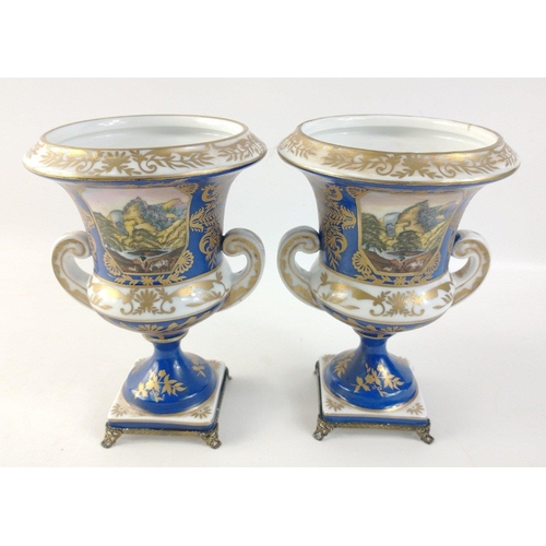 305 - A pair of twin-handled pedestal urns with metallic feet in blue with gilt highlights each standing a... 