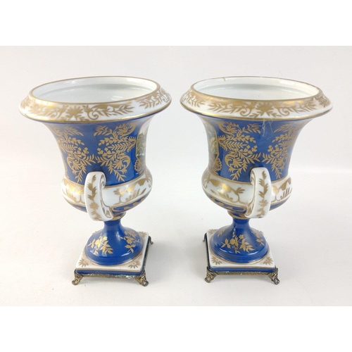 305 - A pair of twin-handled pedestal urns with metallic feet in blue with gilt highlights each standing a... 