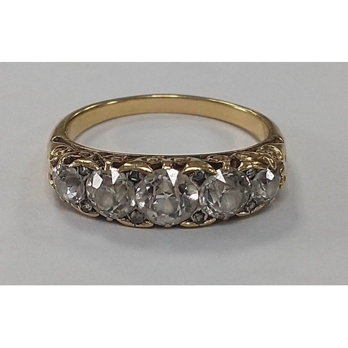 7 - An unmarked yellow metal ring with elaborate shoulder design with 5 mid-cut substantial clear stones... 