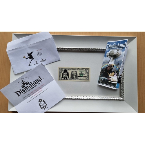 6 - A framed stencilled DISMALAND real One Dollar bill stamped with the BANKSY chomp along with a stenci... 