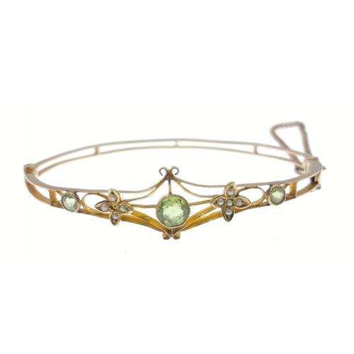 53 - A delicate and unmarked yellow metal snap-shut bangle with safety chain set with peridot stone and s... 