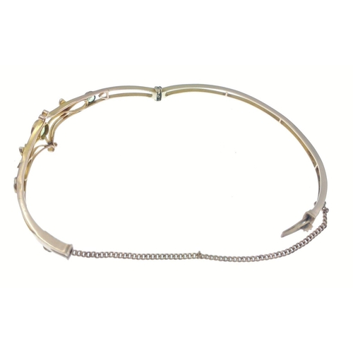 53 - A delicate and unmarked yellow metal snap-shut bangle with safety chain set with peridot stone and s... 