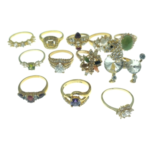 187 - A dozen BLING rings in bright gold style finishes. Assorted sizes and stones.