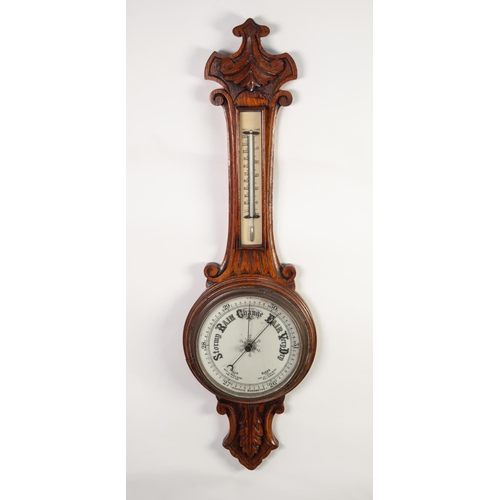 42 - LATE VICTORIAN CARVED OAK ANEROID BAROMETER, the 8” dial set beneath a mercury thermometer to the tr... 