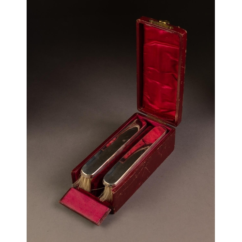 189 - CASED PAIR OF PLAIN SILVER BACKED CLOTHES BRUSHES, each of slender form, housed in red lined and fit... 
