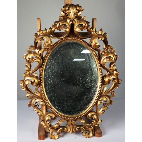 112 - FLORENTINE STYLE CARVED GILTWOOD WALL MIRROR, the oval, mirrored plate within a beaded surround and ... 