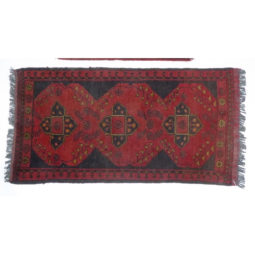 24 - AFGHAN KHAN HAND-WOVEN PURE WOOL RUG, crimson and black with a row of three quatrefoil medallions, n... 