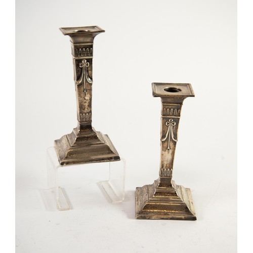 487 - GEORGE V PAIR OF EMBOSSED AND WEIGHTED PRESENTATION SILVER DRESSING TABLE CANDLESTICKS, each of squa... 