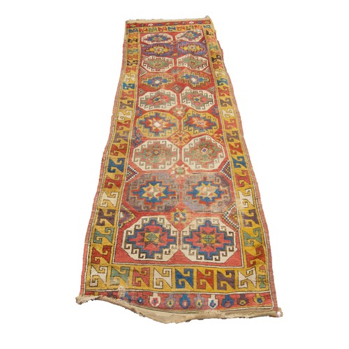 58 - SEMI-ANTIQUE CAUCASIAN RED GROUND RUNNER with eighteen large octagonal guls, each interior with a ce... 