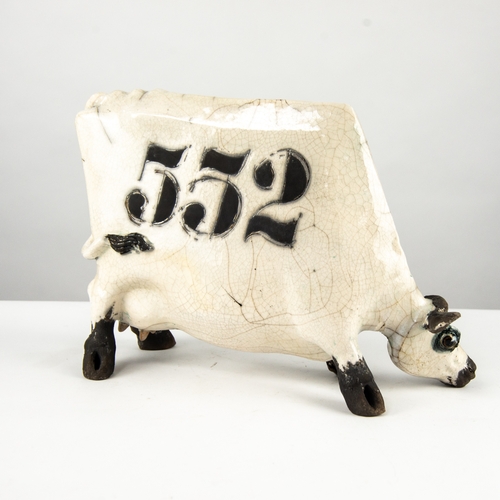 38 - *LANSON E RUDGE (b.1936), A RAKU FIRED STUDIO POTTERY SCULPTURE OF A FLAT COW with a black and white... 