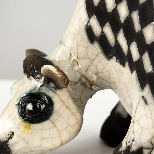 38 - *LANSON E RUDGE (b.1936), A RAKU FIRED STUDIO POTTERY SCULPTURE OF A FLAT COW with a black and white... 