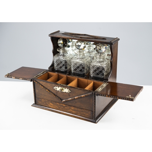 83 - CIRCA 1920's OAK TANTALUS with THREE SQUARE CUT GLASS DECANTERS, having a spring-release games drawe... 