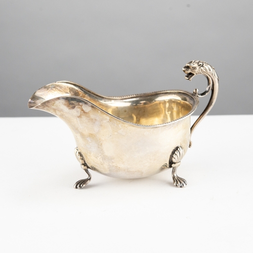 322 - INTER-WAR YEARS SILVER SAUCE BOAT with gadrooned rim and lion-headed flying scroll handle, on three ... 