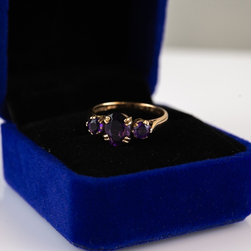 65 - 9ct GOLD RING claw set with a centre oval amethyst and flanking round amethysts, 2.7gms, ring size '... 