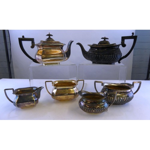 354 - TWO THREE PIECE ELECTROPLATED TEA SETS, with black angular scroll handles, one of part fluted form, ... 