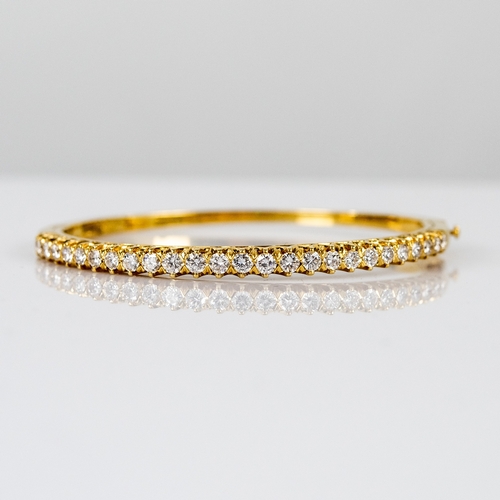 27 - GOLD AND DIAMOND HINGE-OPENING BANGLE, the top claw set with a half hoop of 26 round, brilliant cut ... 