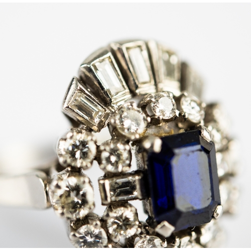 44 - PLATINUM, SAPPHIRE AND DIAMOND THREE TIER CLUSTER RING set with a centre emerald-cut blue sapphire, ... 