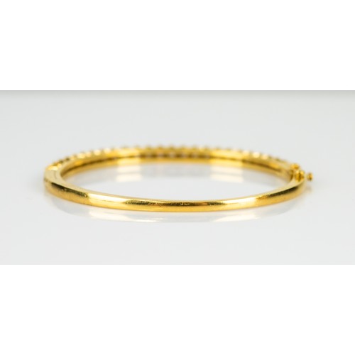 27 - GOLD AND DIAMOND HINGE-OPENING BANGLE, the top claw set with a half hoop of 26 round, brilliant cut ... 