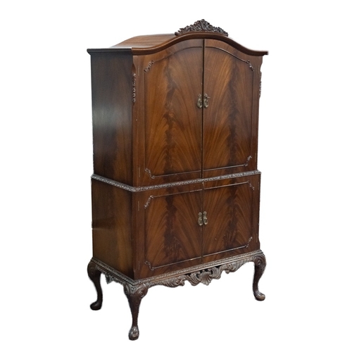 81 - CAROLEAN STYLE MODERN FLAME CUT MAHOGANY DRINKS CABINET, the arched top with pierced, floral crestin... 