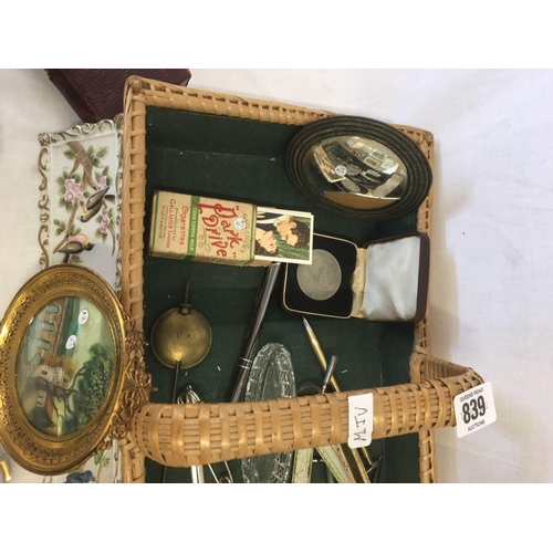 839 - SMALL CANE BASKET WITH MISC METALWARE, HORN COMB, CHINA PIN DISHES, CALLIGRAPHY PEN & 2 GILT FRAMED ... 