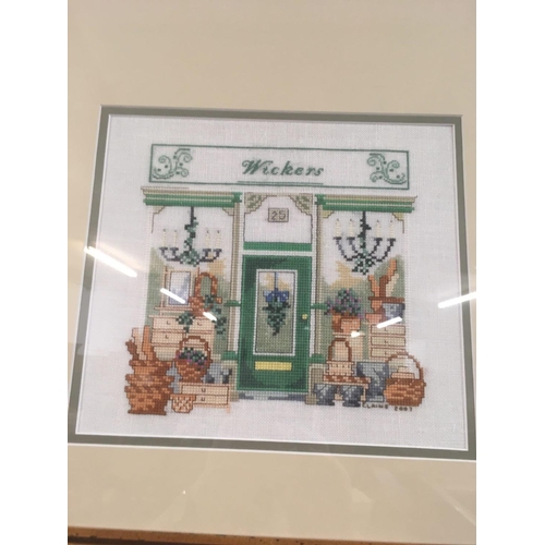 559 - FRAME CONTAINING 3 NEEDLEWORK PICTURES OF SHOP FRONTS, 2 INDISTINCTLY SIGNED, 23'' X 44''