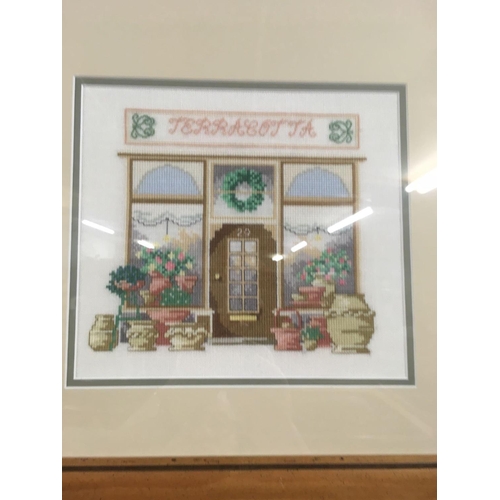 559 - FRAME CONTAINING 3 NEEDLEWORK PICTURES OF SHOP FRONTS, 2 INDISTINCTLY SIGNED, 23'' X 44''