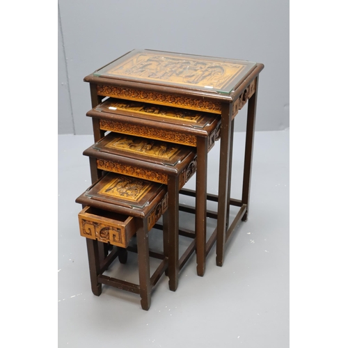 566 - A Nest of Four Carved Hardwood Glass Topped Oriental Tables, With Each Table Depicting Different Sce... 