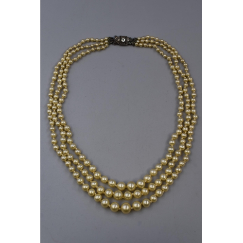 77 - A Sterling Silver Clear Stoned Clasped Three Strand Pearl Necklace. In Presentation Box