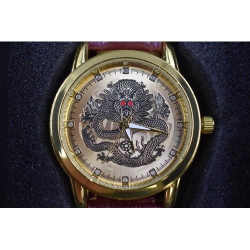 108 - An Oriental Dragon Style Gold Tone Faced Watch With Red Leather Strap, In Presentation Box