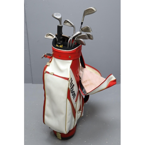 735 - A set of Syncron right handed golf clubs in a Wilson golf bag with umbrella and accessories. No Post... 