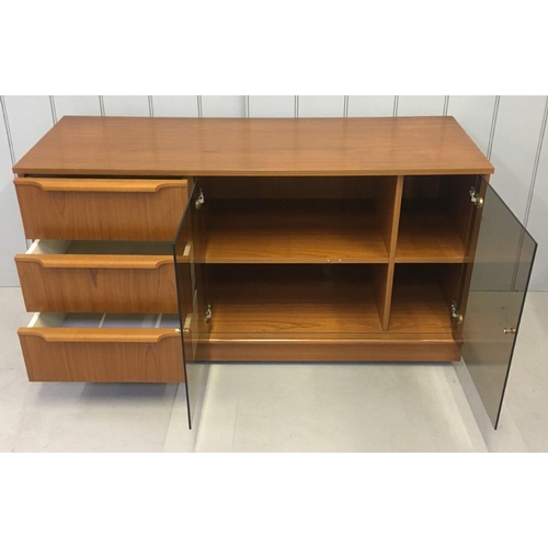 118 - A mid-century, teak coloured TV/Hi-Fi Cabinet. Glass doored, two-shelved, three drawers, on castors.... 