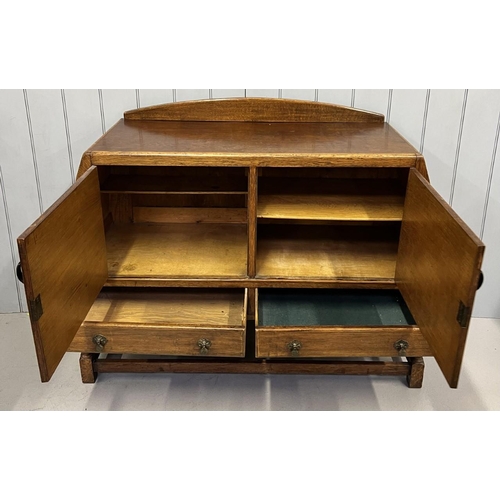 51 - An Arts & Crafts oak sideboard. Double cupboard over two drawers. Decorative iron hinges & handles. ... 