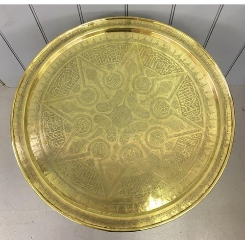 23 - A vintage large, engraved, Indian brass tray-table, with folding legs. Height 58cm, diameter 64cm.