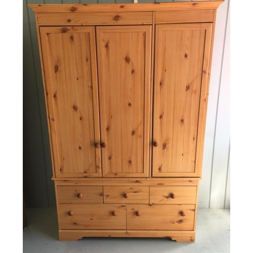 57 - A modern, pine-effect triple wardrobe. Three doors, two hanging rails, three narrow drawers over two... 