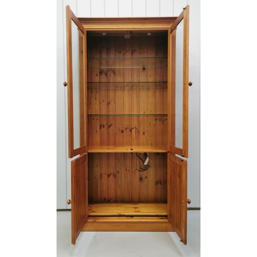 1002 - A tall pine & glazed display cabinet. Three glass shelves to display area, over double cupboard. Dis... 