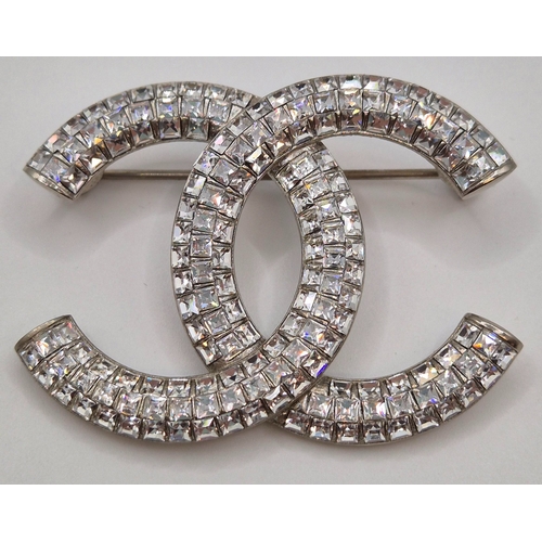 1703 - Chanel white metal/crystal-set brooch in the form of  interlocking C's logo. Complete with original ... 