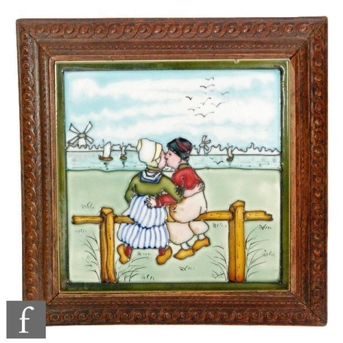 114 - A framed 8in tile decorated with a tubelined Dutch scene with a lady and gentleman kissing whilst lo... 