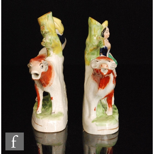 109 - A mirrored pair of Staffordshire spill vases modelled as facing cows with a lady and gentleman stood... 