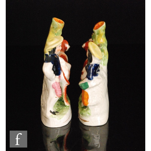 109 - A mirrored pair of Staffordshire spill vases modelled as facing cows with a lady and gentleman stood... 