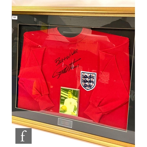 1693 - A framed England red football shirt signed ‘Best wishes Geoff Hurst’, inset with photograph of Geoff... 