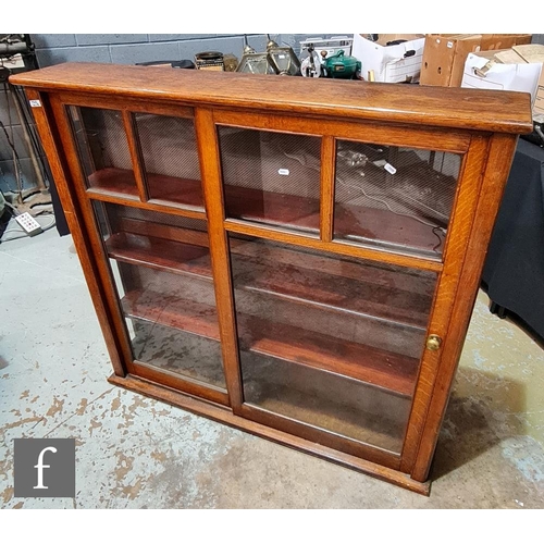 1230 - A 1930s office oak display cabinet enclosed by a pair of bar glazed sliding doors on a plinth base, ... 