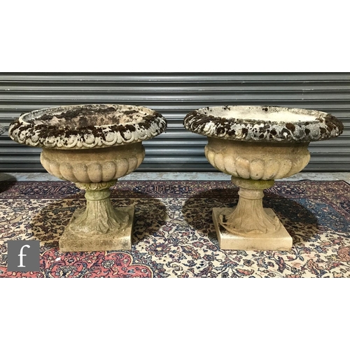 1245 - A pair of composite stone terrace vases each of half fluted form on leaf spreading square plinth bas... 