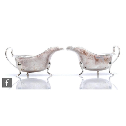 20 - A pair of hallmarked silver sauce boats each raised on three pad feet and terminating in scroll hand... 