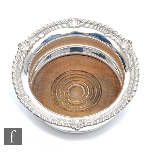 58 - A hallmarked silver bottle coaster of plain form with wooden base and gadroon and leaf border, diame... 