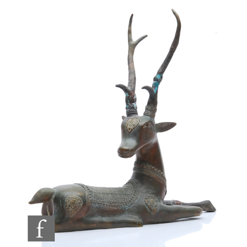 180 - A Tibetan/Himalayan cast metal figure of a recumbent stag, head alert and turned with a foreleg outs... 