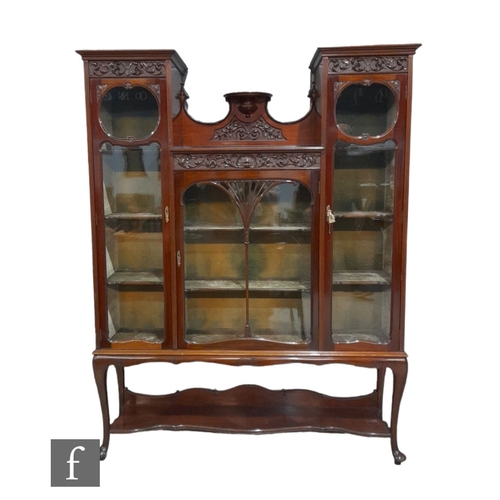 984 - An Edwardian triple door mahogany display cabinet enclosed by glazed doors with carved panelled fron... 