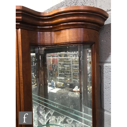 991 - A late 20th Century walnut finish floorstanding serpentine glazed display cabinet enclosed by a sing... 